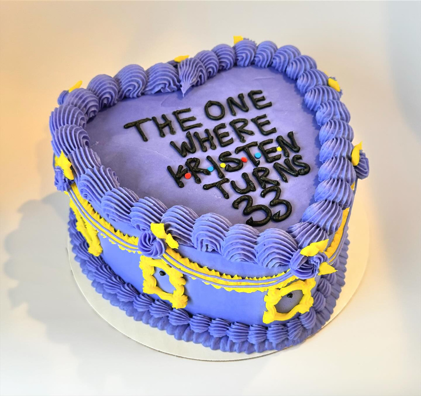 A heart-shaped custom 8 inch buttercream cake decorated in the theme of the hit TV show "Friends".  It features lambeth-style piping of the iconic frame on the purple door, and custom wording on top to match the Friends logo.