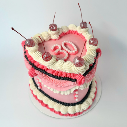 A heart-shaped cake in a vintage theme, with pink black and white ornate piping, glitter-dipped cherries, and white pearls spelling out "30" on top.